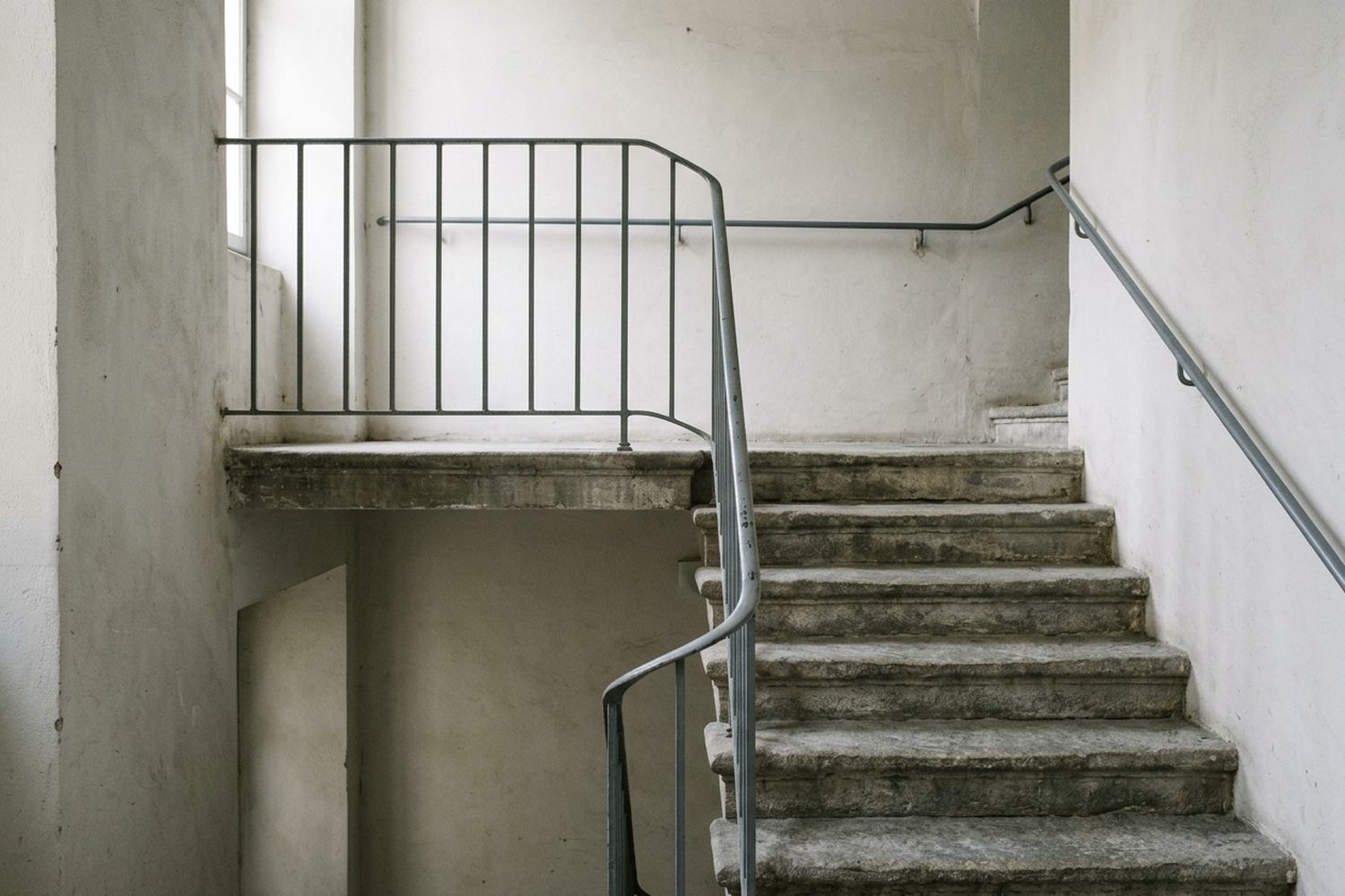 A stone stair turning on a half landing under a plain rail.