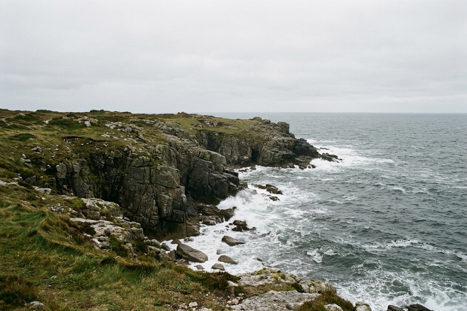 Low granite cliffs above cold open water under flat cloud.