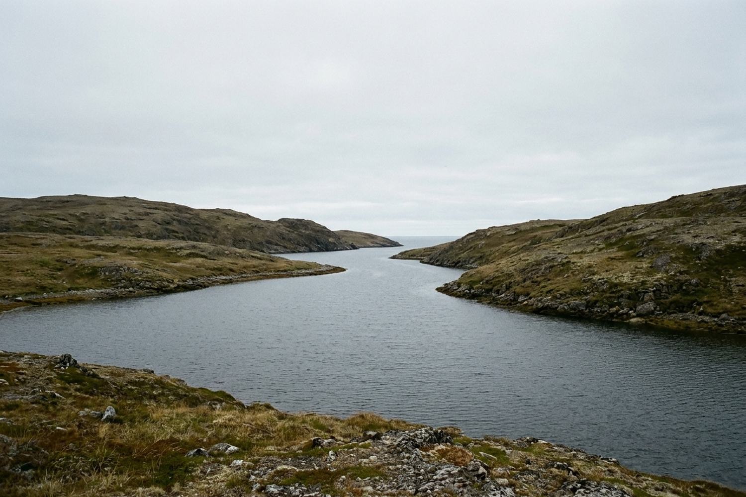 A narrow sea inlet between low treeless hills.